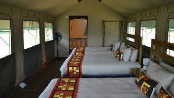 A tented accommodation with two beds, each with a quilted blanket and pillows.