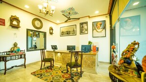 A reception area with a desk, chairs, a clock, and a ceiling fan. - Hotel Radhika Jaisalmer (Jaisalmer)