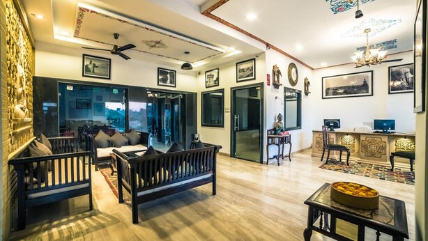 A spacious living area with a sofa, a coffee table, and a dining table. There are framed pictures on the walls and a ceiling fan. - Hotel Radhika Jaisalmer (Jaisalmer)