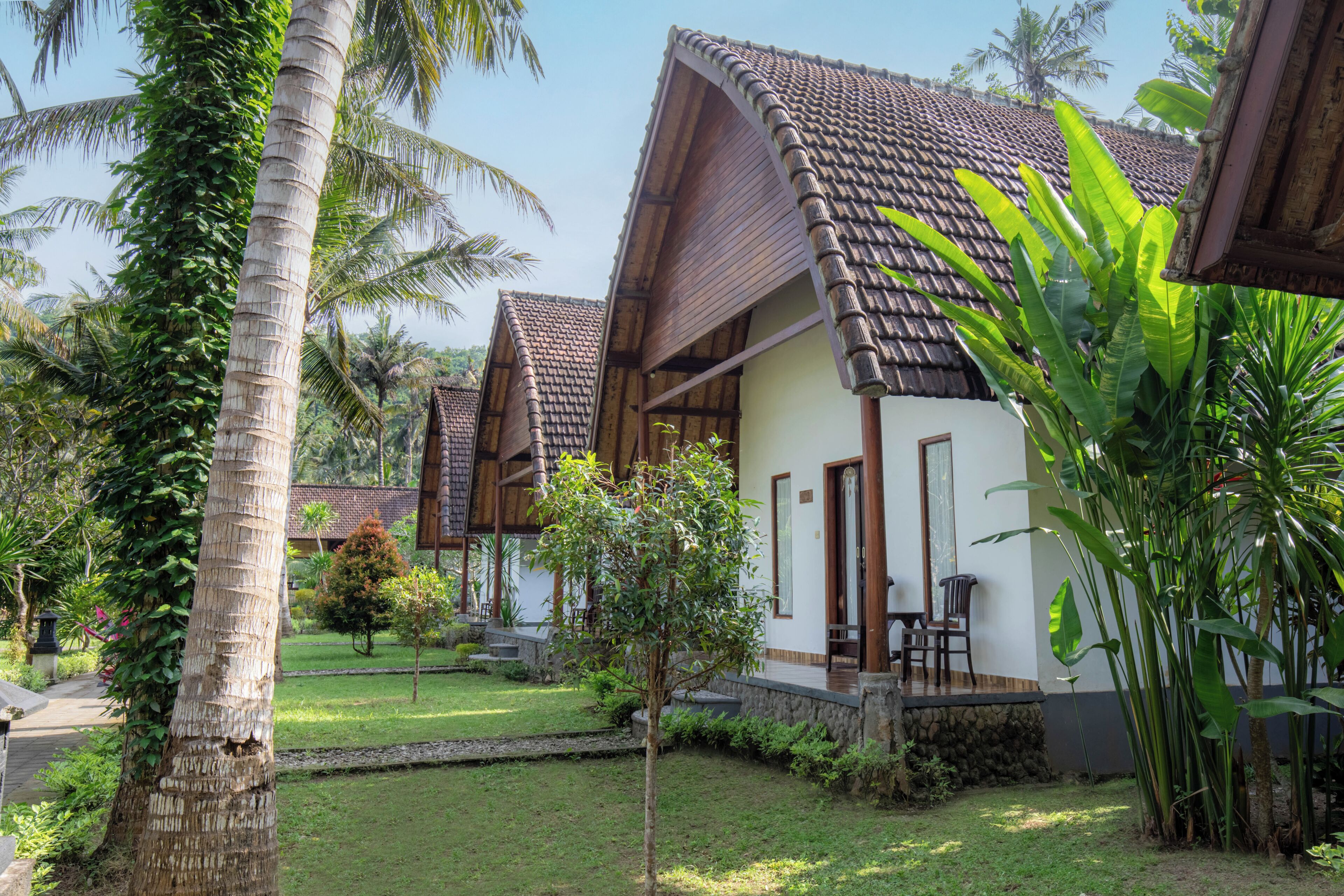 A bungalow with a tiled roof, surrounded by lush greenery and palm trees.