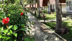 A pathway lined with palm trees and red hibiscus flowers leading to a building with a tiled roof. - Crystal Bay Villa (Penida Island)