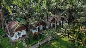 A row of bungalow-style accommodations with thatched roofs, surrounded by lush greenery and palm trees. - Crystal Bay Villa (Penida Island)