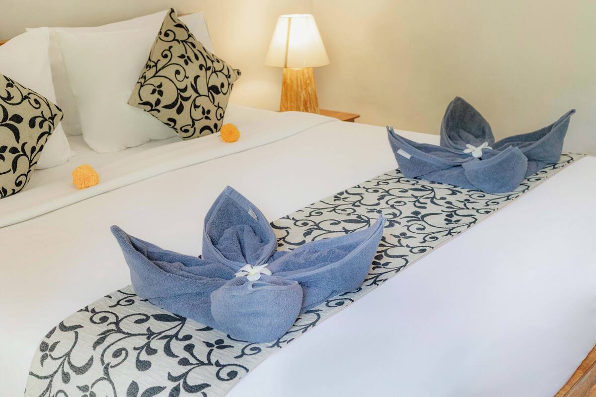 A neatly made bed with decorative towels and a patterned runner.