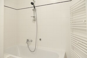 A modern bathroom with a bathtub, a showerhead, and a white tiled wall.