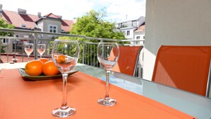 Een balkon met een tafeltje, twee wijnglazen, een bord sinaasappels en een glas water.