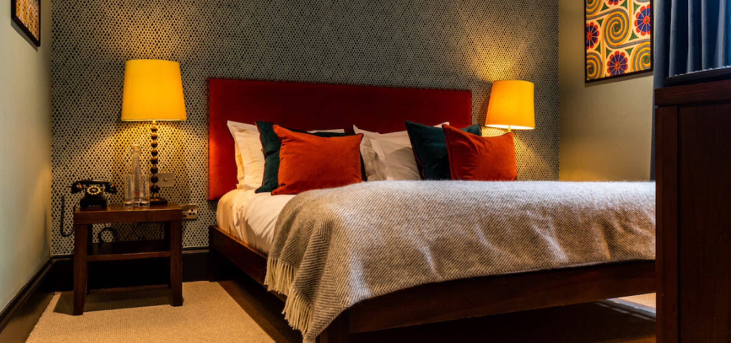 A neatly made bed with a red headboard, two bedside lamps, and a patterned wall.