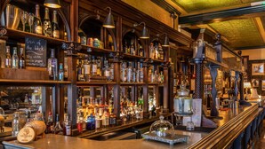Un bar con estantes llenos de botellas y vasos diversos, un menú en una pizarra y una barra de madera.