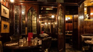Un restaurante tenuemente iluminado con decoración de madera y suelo a cuadros. Las mesas están dispuestas con vasos y cubiertos.
