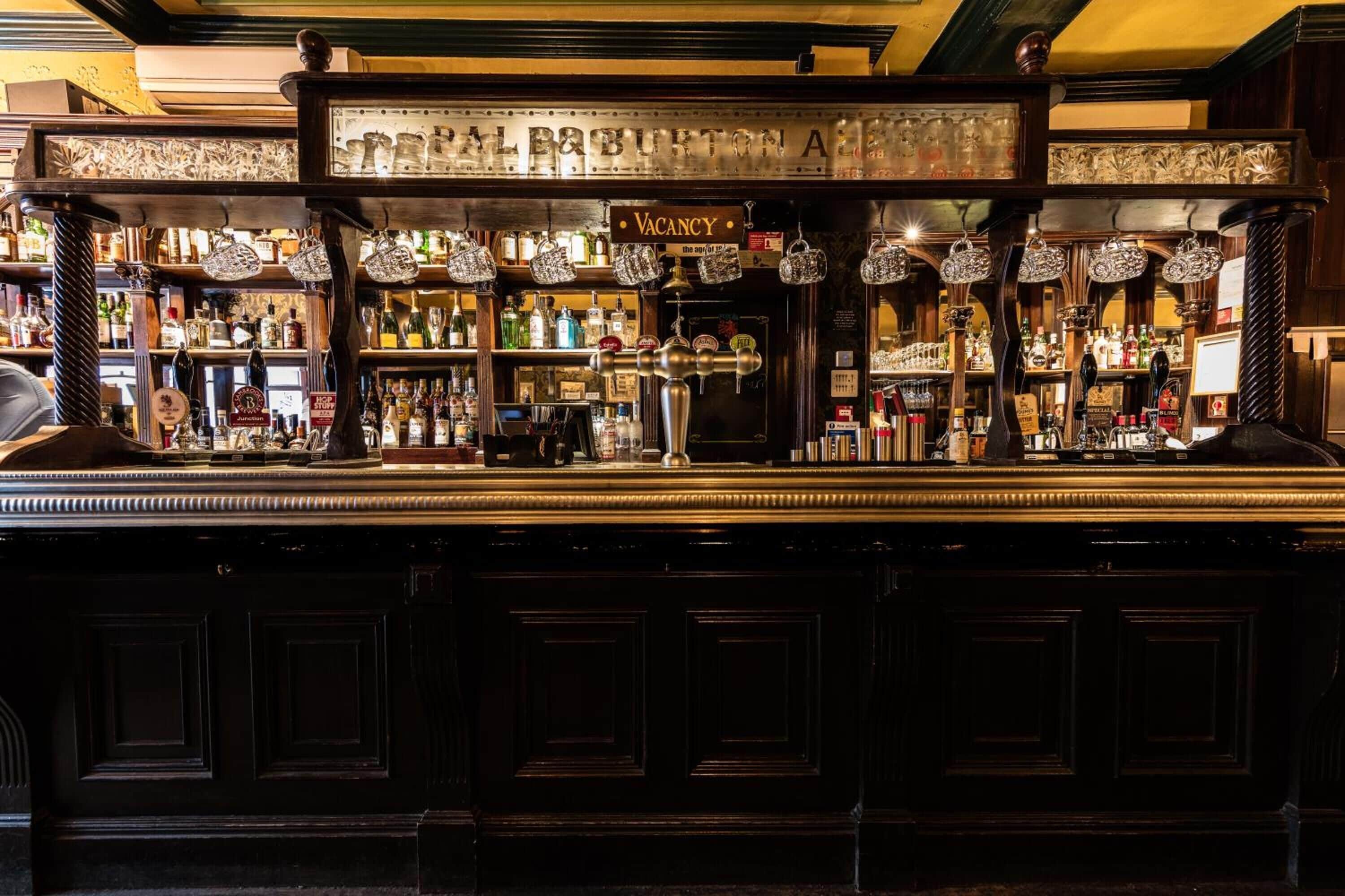 Un bar con un letrero de 'VACANCY', estantes llenos de botellas y una llave para cerveza.