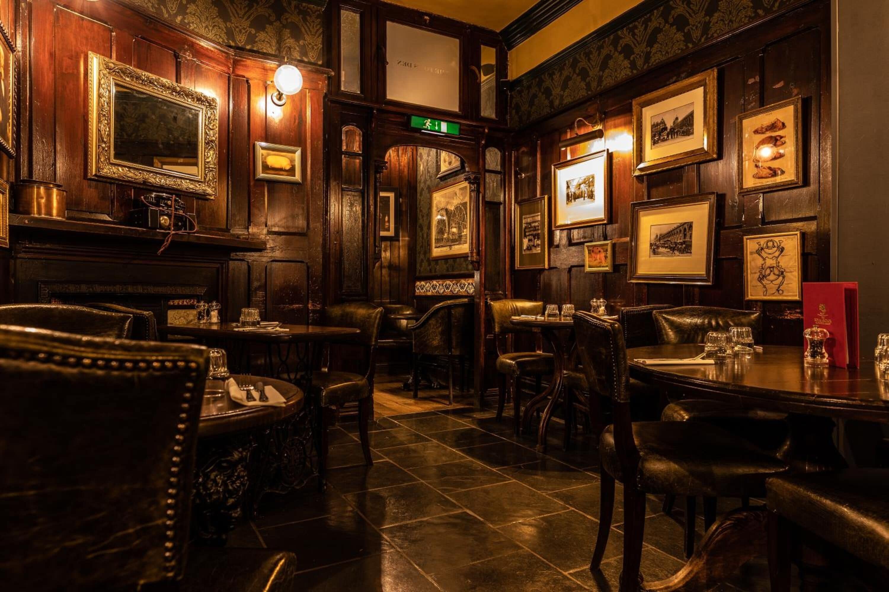 Un restaurante con poca luz, paneles de madera, cuadros en las paredes y sillas de cuero.