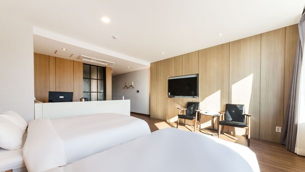 A modern hotel room with two beds, a desk, a TV, and a seating area with chairs. - Incheon Hotel Bluemarine (Incheon)
