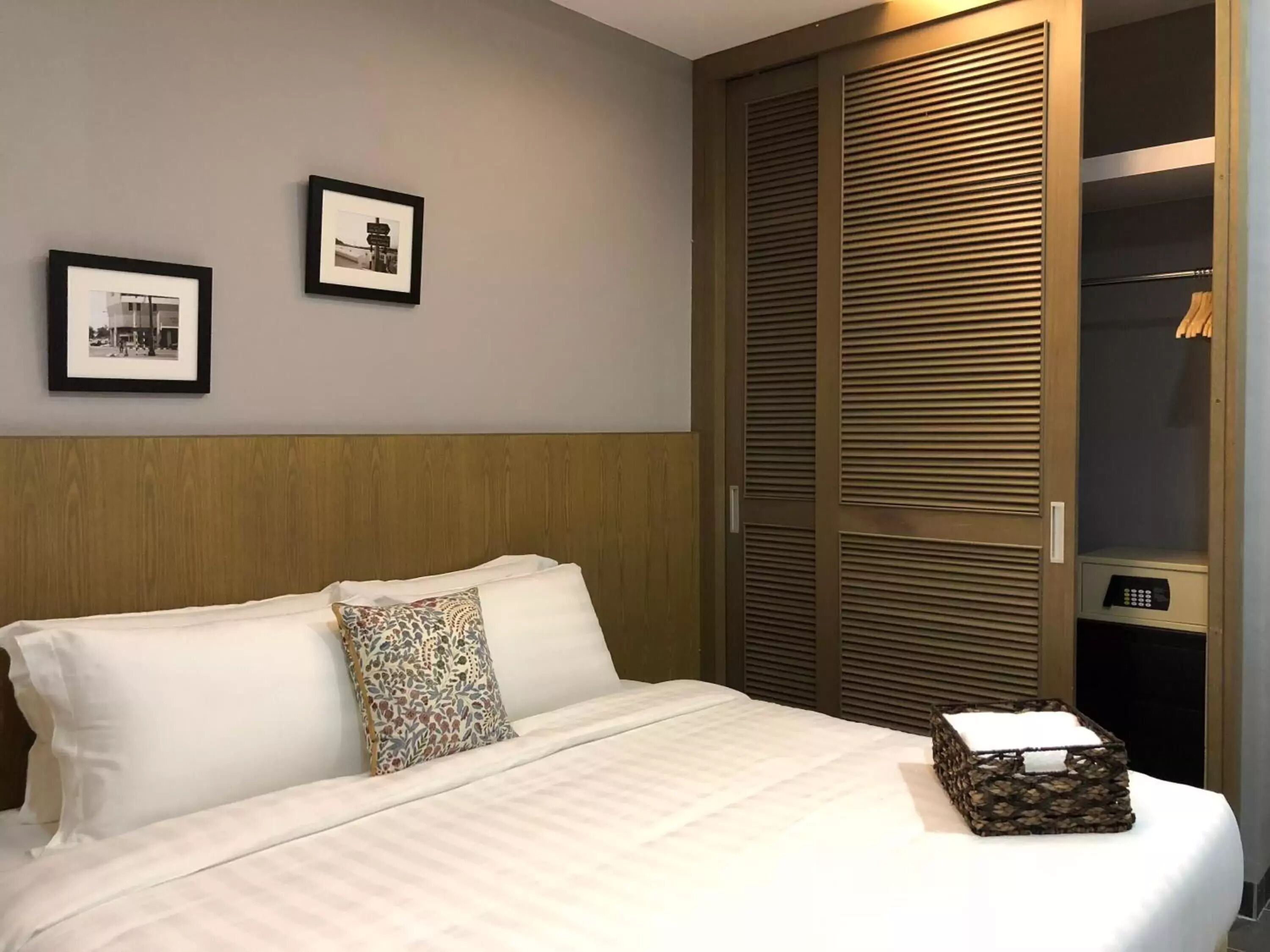 A hotel room with a bed, two framed pictures on the wall, and a wooden wardrobe with a control panel.
