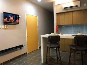 A small kitchenette with a TV, a door, and two bar stools. - Telanai16 Lodge (Bandar Seri Begawan)