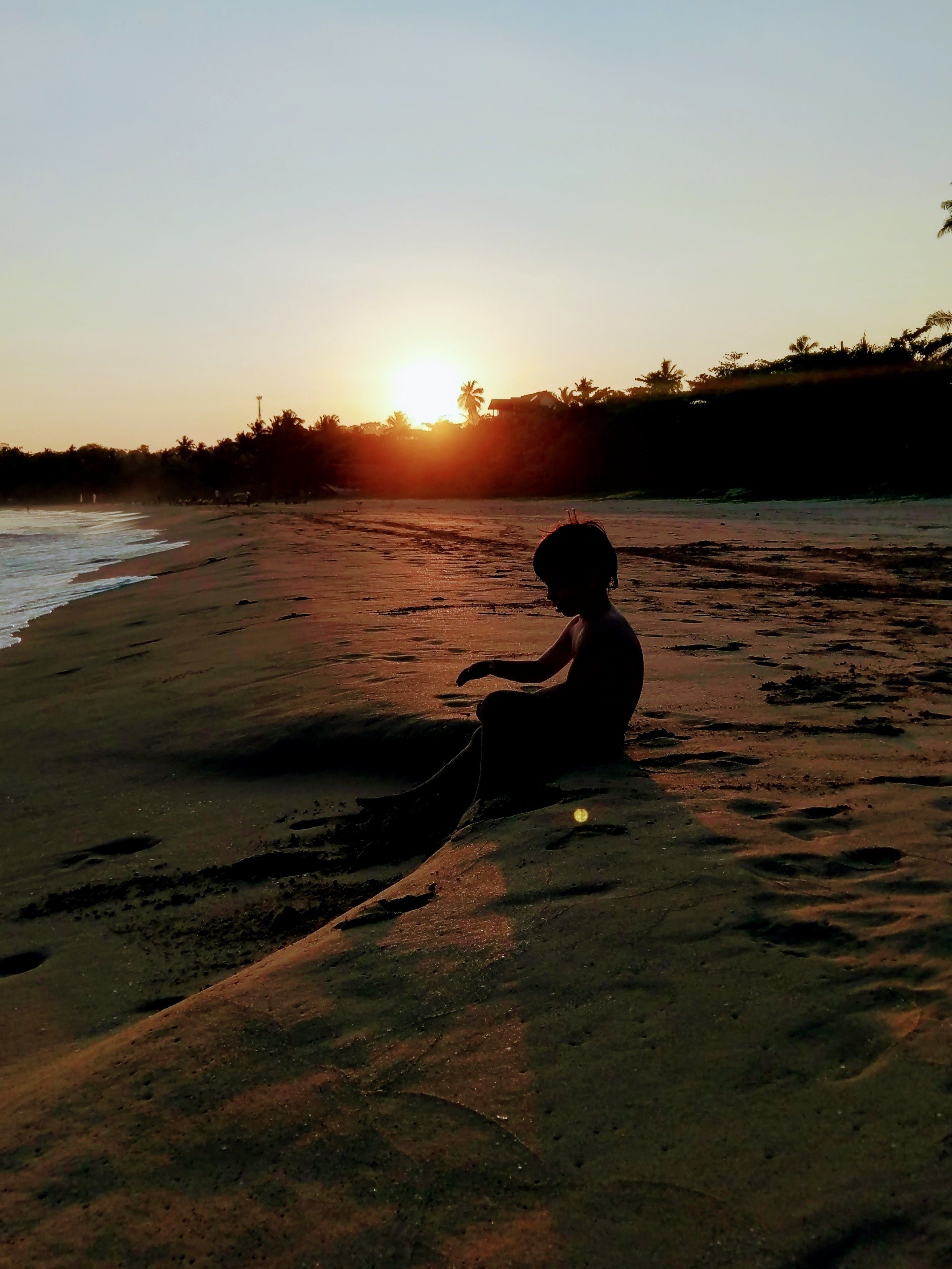 Silueta de una persona sentada en una playa arenosa al atardecer.