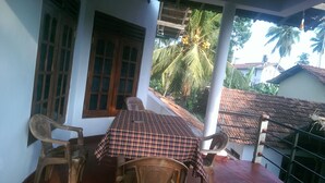 A room with a checkered table, two chairs, a window with wooden shutters, and a view of a residential area with palm trees. - Paradise Beach House (Talalla)