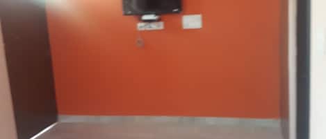 Una habitación con una pared naranja, un televisor de pantalla plana montado en la pared, una cama con ropa blanca y un tapete verde en el suelo.