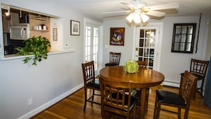 A dining room with a wooden table and chairs, a ceiling fan, and a kitchen area with a microwave and shelves. - City's Escape (Pemberton)