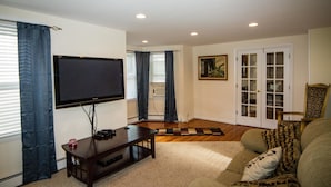 A living room with a flat-screen TV, a wooden coffee table, a patterned rug, a sofa with cushions, and a door leading to a closet. - City's Escape (Pemberton)