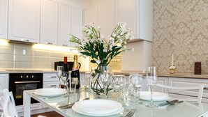 A modern kitchen with white cabinetry, a glass dining table set with white plates, silverware, and wine glasses. - Homestay Apartments (Chisinau)