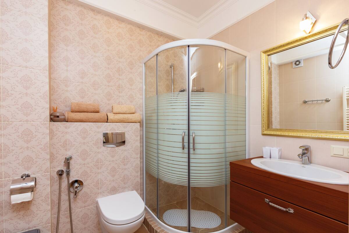 Un baño moderno con ducha de vidrio, inodoro blanco, tocador de madera con espejo y barra para toallas.