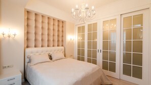 A bedroom with a tufted headboard, a chandelier, a large bed, and a wardrobe with frosted glass doors. - Homestay Apartments (Chisinau)