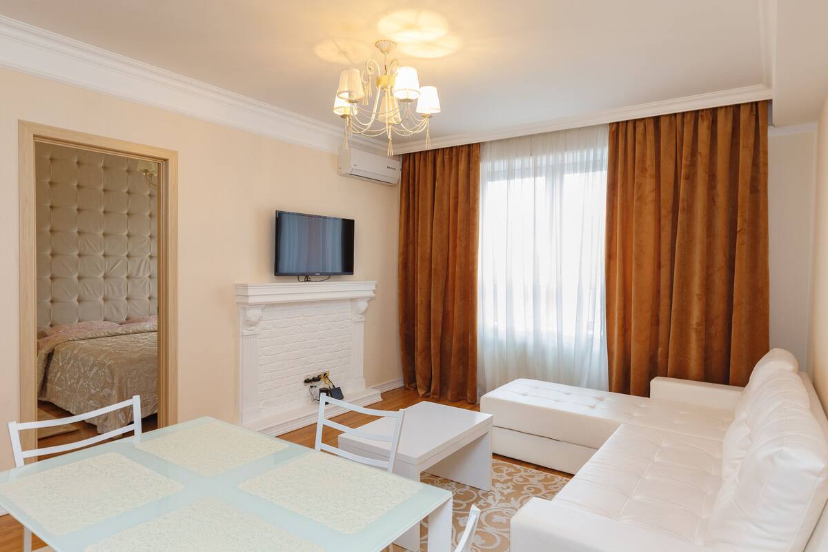 Una sala de estar moderna con un sofá blanco, una mesa con cubierta de vidrio, una chimenea blanca y un televisor montado en la pared.