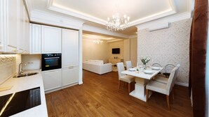 A modern kitchen with white cabinetry, a built-in oven, and a dining area with a white table and chairs. - Homestay Apartments (Chisinau)