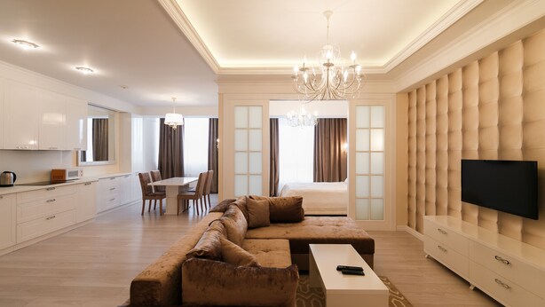 A modern living room with a sectional sofa, a flat-screen TV, and a dining area with a chandelier. - Homestay Apartments (Chisinau)