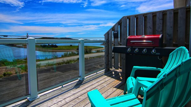 A wooden deck with a grill and turquoise chairs overlooking a body of water. - The Killick Inn & Suites (Arnold's Cove)