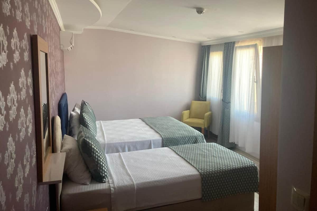 A hotel room with two beds, a chair, a mirror, and a window with curtains.
