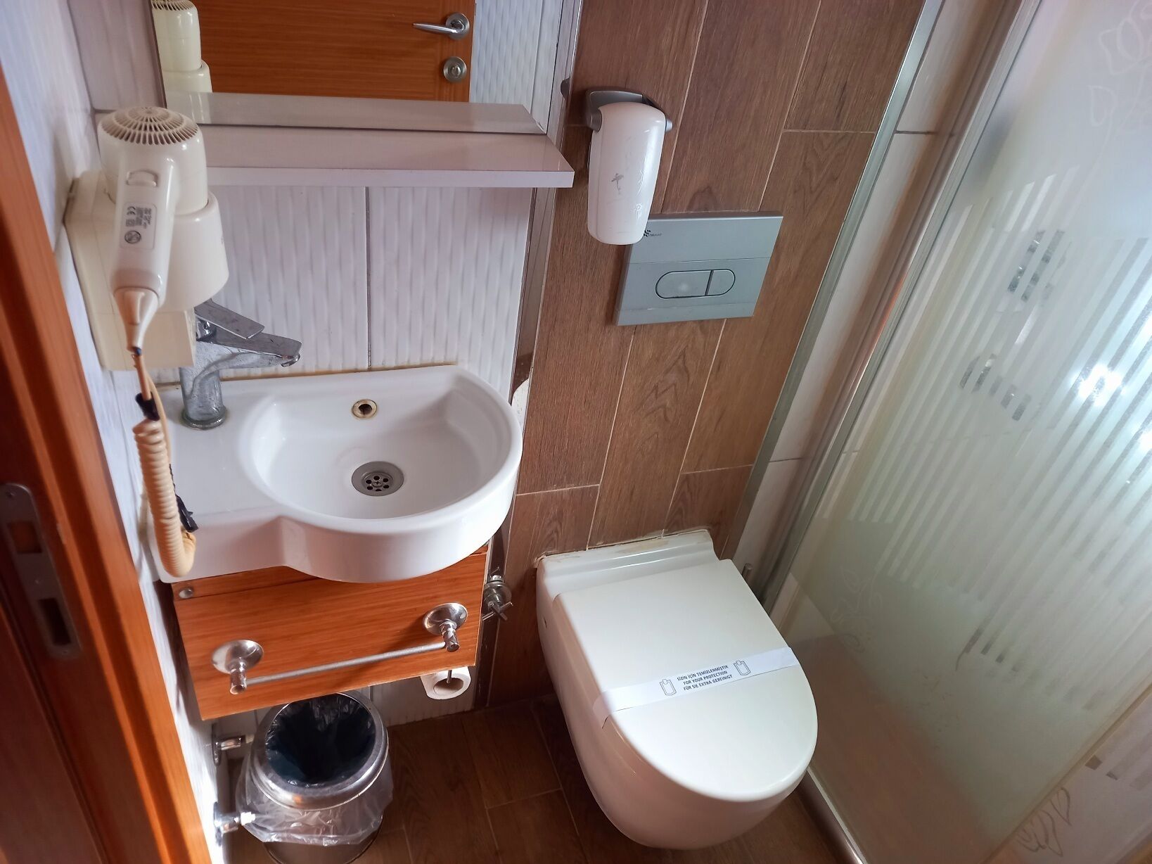 A compact bathroom with a sink, toilet, and a hairdryer on the wall.