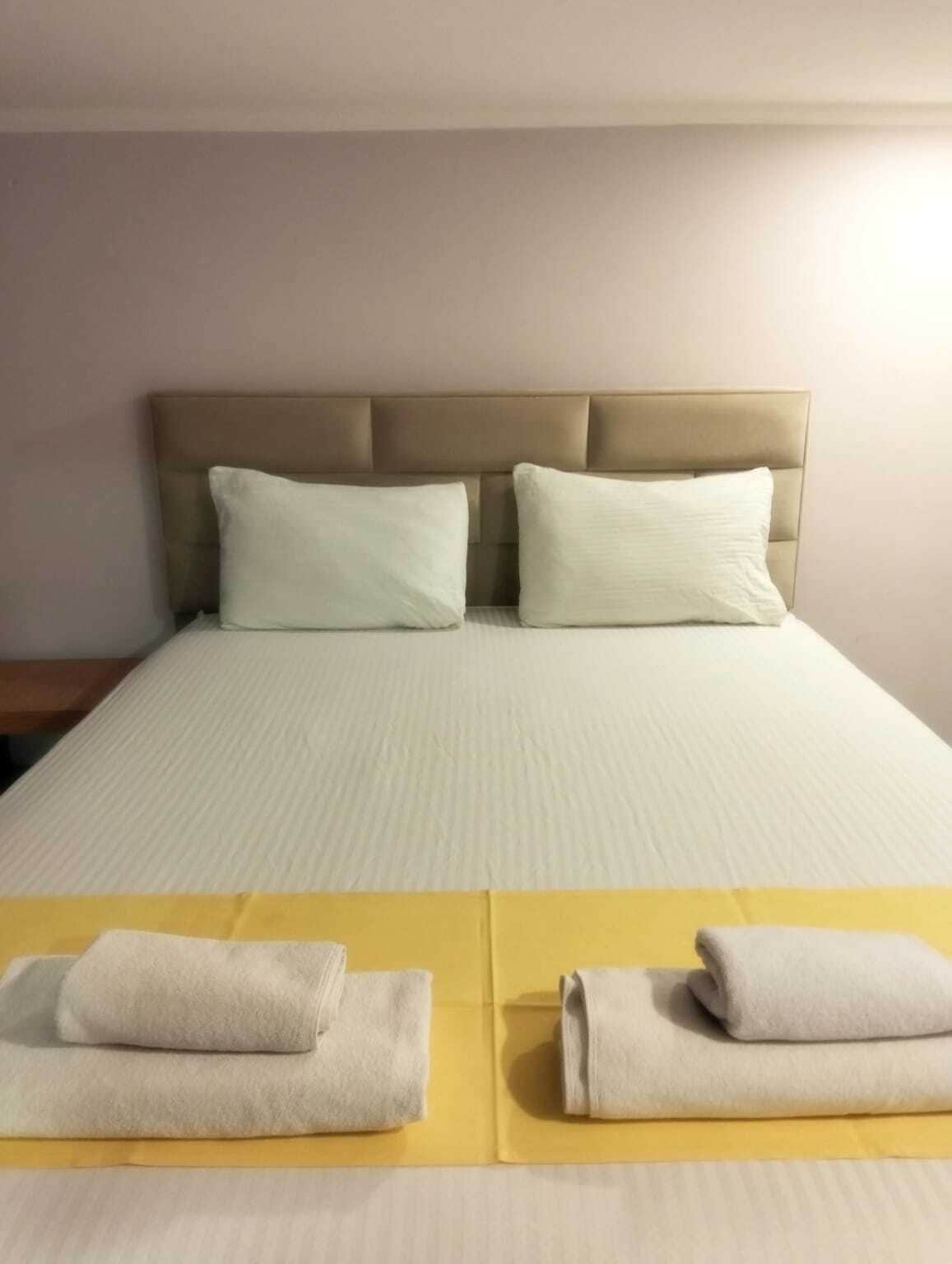 A bed with a headboard, two pillows, and two folded towels on a yellow mat.