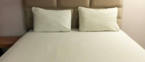 A bed with a headboard, two pillows, and two folded towels on a yellow mat.