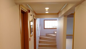 A clean, well-lit hallway with a wooden door, a window, and a staircase leading to another floor. - Otel Safran Palas (Foça)