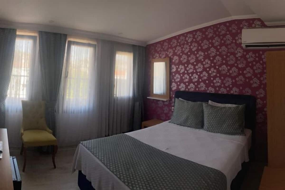 A hotel room with a bed, a chair, a desk, and a window with curtains.