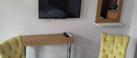 A room with a television mounted on the wall, a small wooden table, and two yellow armchairs.