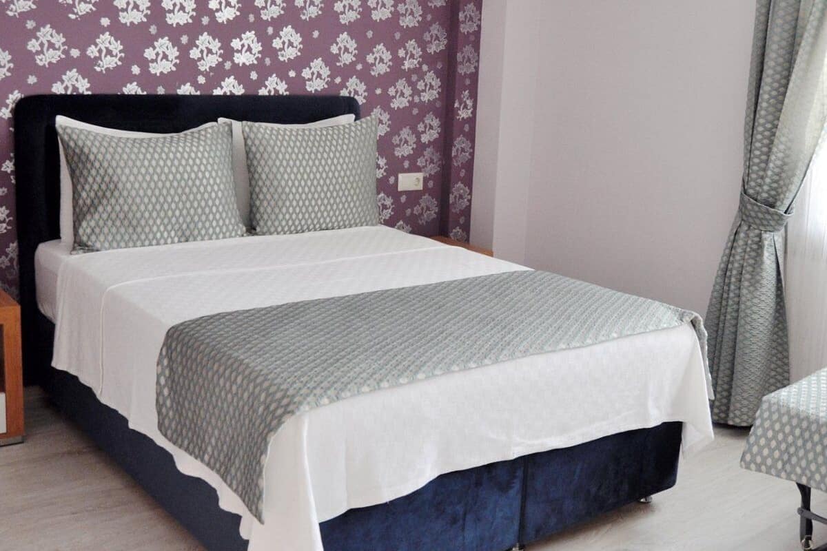 A bed with a dark headboard, two pillows, a grey and white bedspread, and a matching grey and white throw.