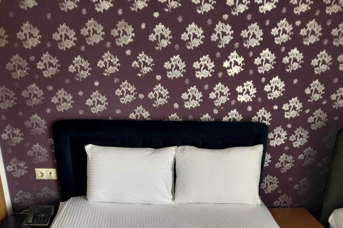 A neatly made bed with white linens and two pillows, a dark headboard, and a patterned wall in the background.