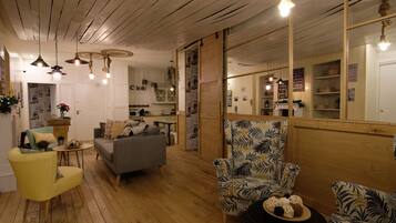 A cozy living room with wooden flooring, a grey sofa, a yellow armchair, and a patterned armchair. There is a small round table with decorative items.