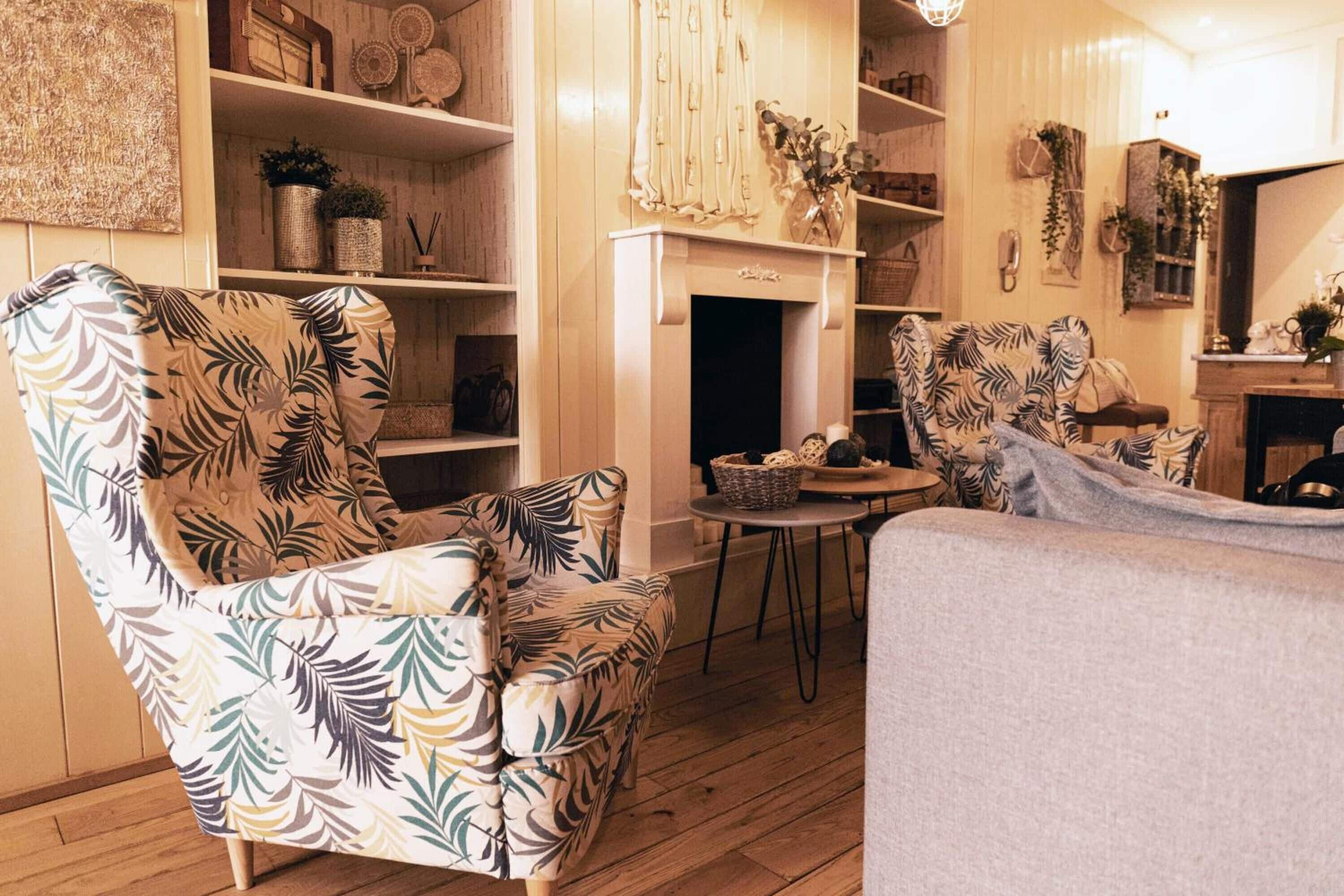 Una sala de estar acogedora con chimenea, un sillón estampado, un sofá y una pequeña mesa redonda.