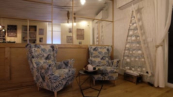 Una habitación acogedora con paredes de madera, dos sillones estampados, una mesita con un adorno y un árbol de Navidad.