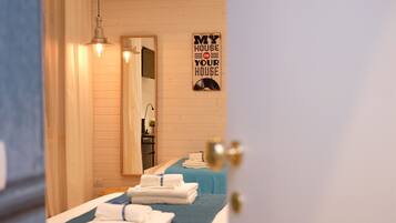Habitación de hotel con dos camas, cada una con cubrecama azul y toallas blancas. Hay un cartel en la pared que dice 'MY HOUSE IS YOUR HOUSE'.