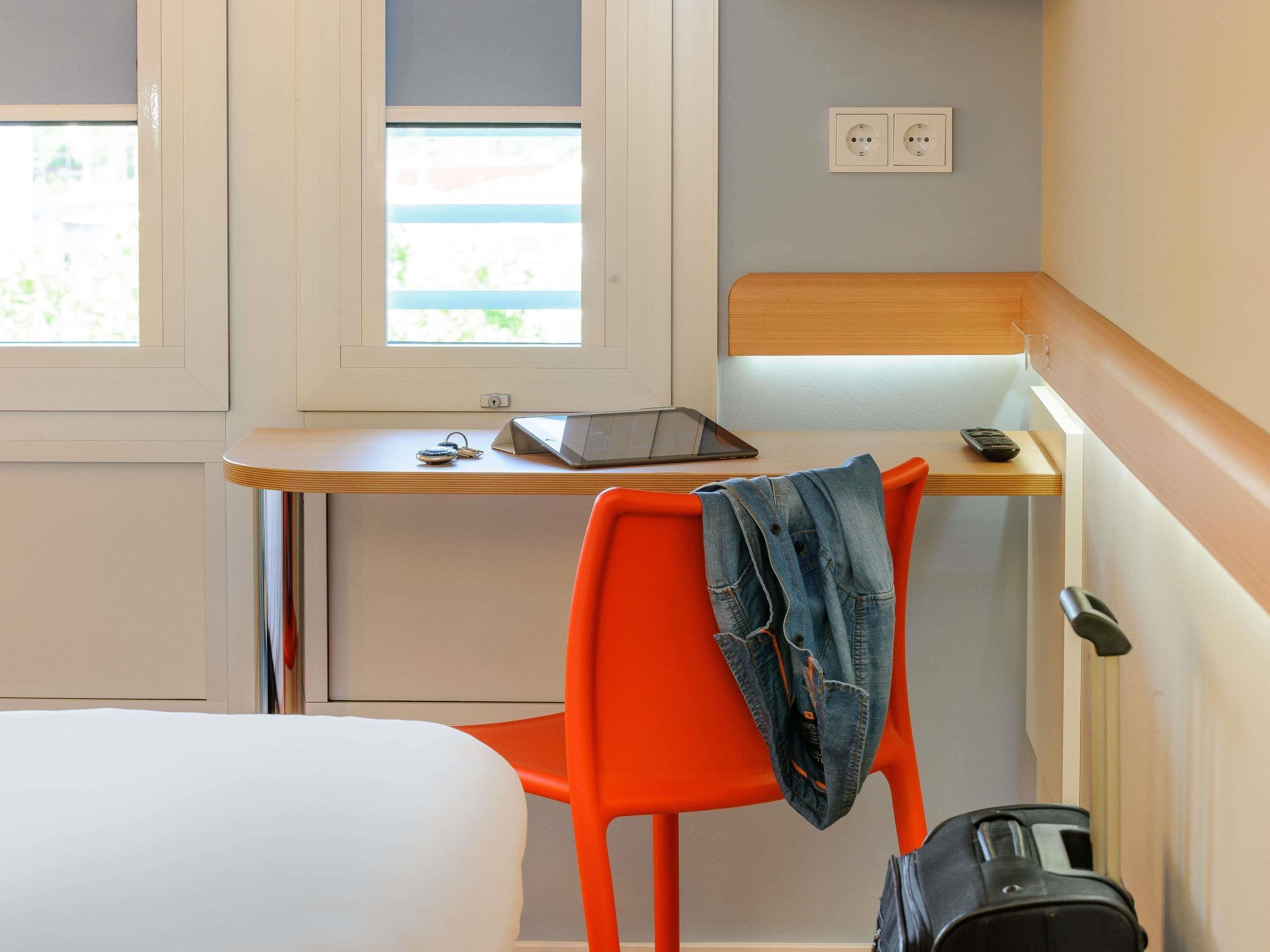 A room with a bed, a desk with a laptop, a chair, and a suitcase.