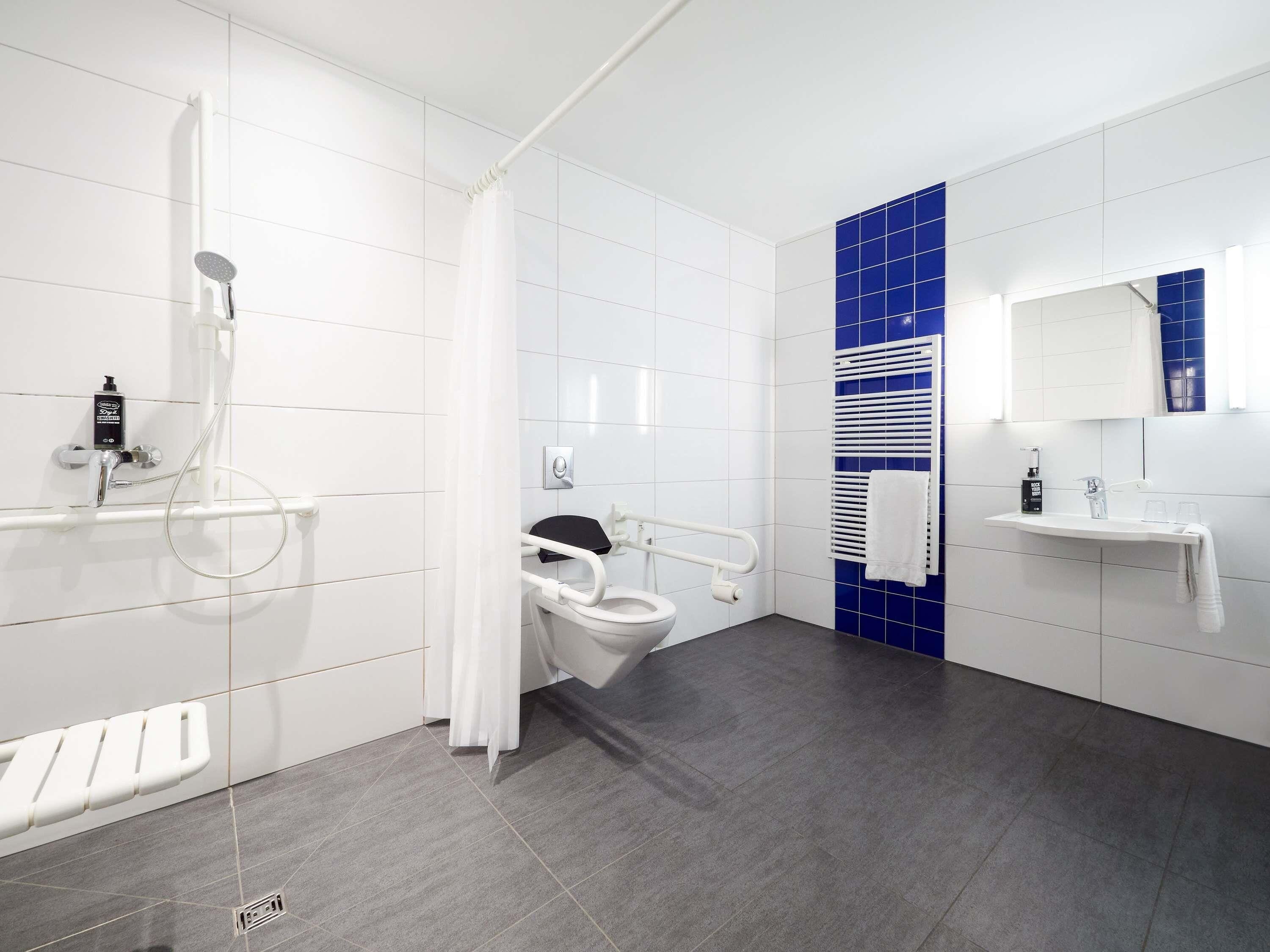 A modern bathroom with a shower, toilet, and sink, equipped with a handrail and a towel rack.