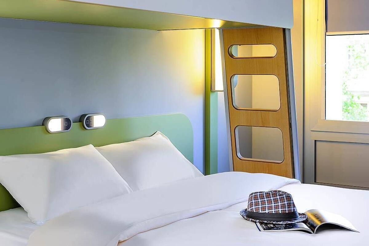 Un lit bien fait, avec des draps blancs, un chapeau à carreaux et un livre posé sur le lit.