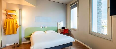 A modern hotel room with a bed, a desk, a chair, a TV, and a large window.