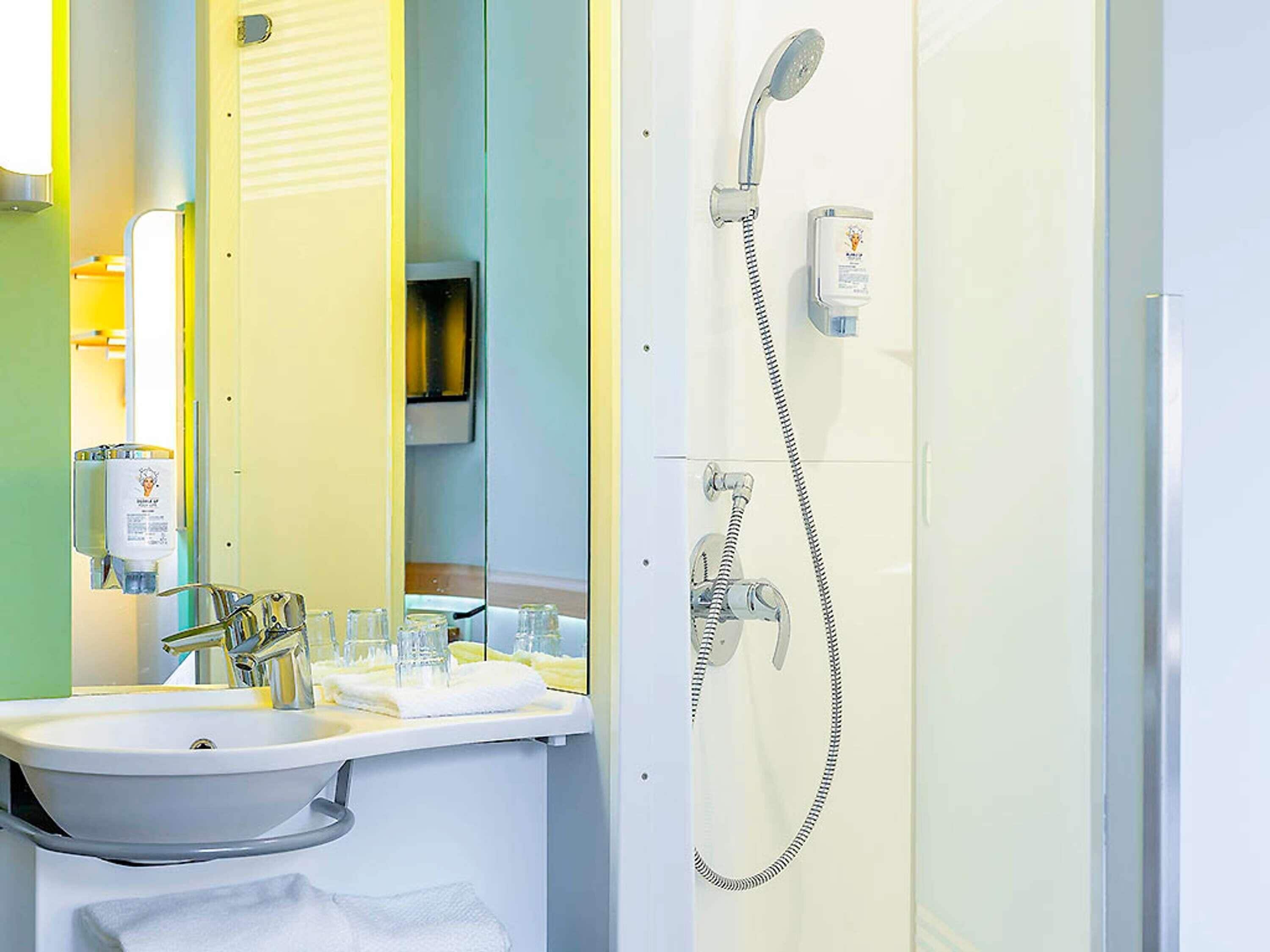 Un baño con lavamanos, espejo, ducha y toallero.