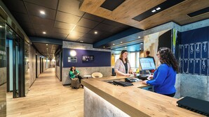 A modern reception area with a wooden reception desk, a seating area, and a digital display. - ibis budget Frankfurt City Ost (Frankfurt)