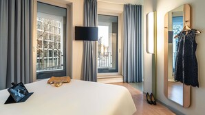 A modern hotel room with a large bed, a flat-screen TV, a mirror, and a view of the city through large windows. - ibis budget Frankfurt City Ost (Frankfurt)