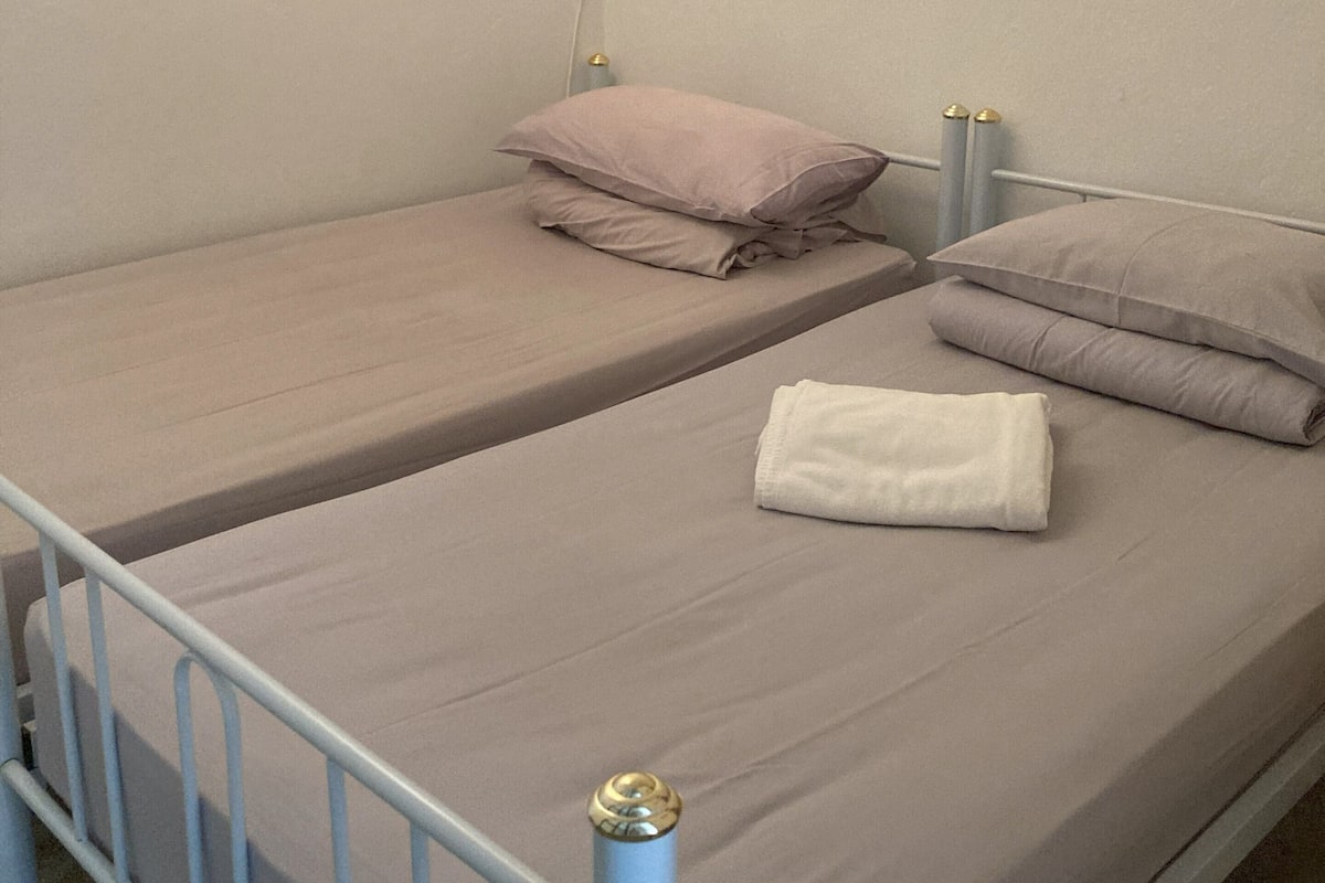 Un lit simple avec un cadre en métal, deux oreillers et une serviette pliée.